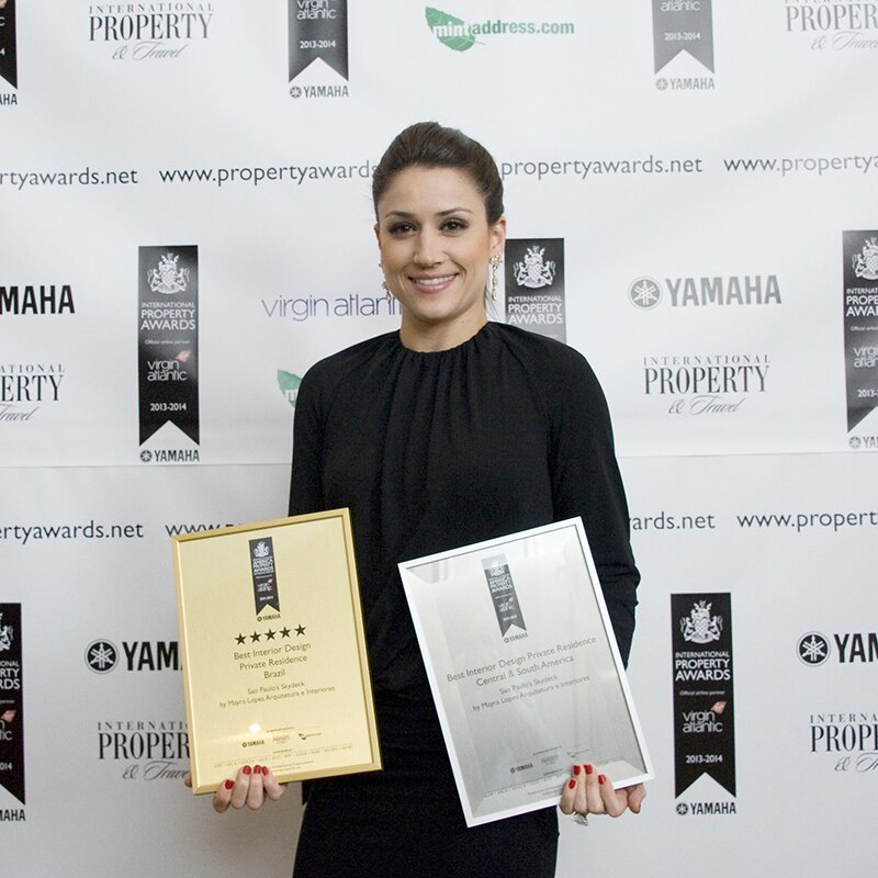 Mayra Lopes com os dois certificados emoldurados — Best Interior Design Private Residence Brazil (5 estrelas) e Central & South America — Americas Property Awards 2013-2014